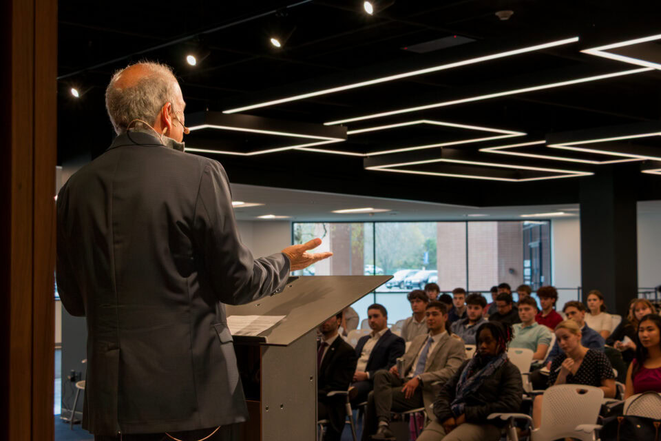 A male speaker addresses students from a podium.