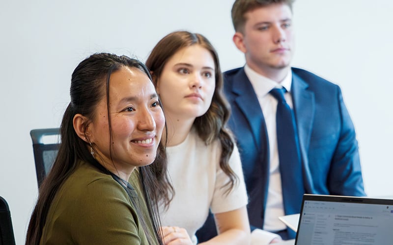 Three students listen to an instructor in a classroom setting.