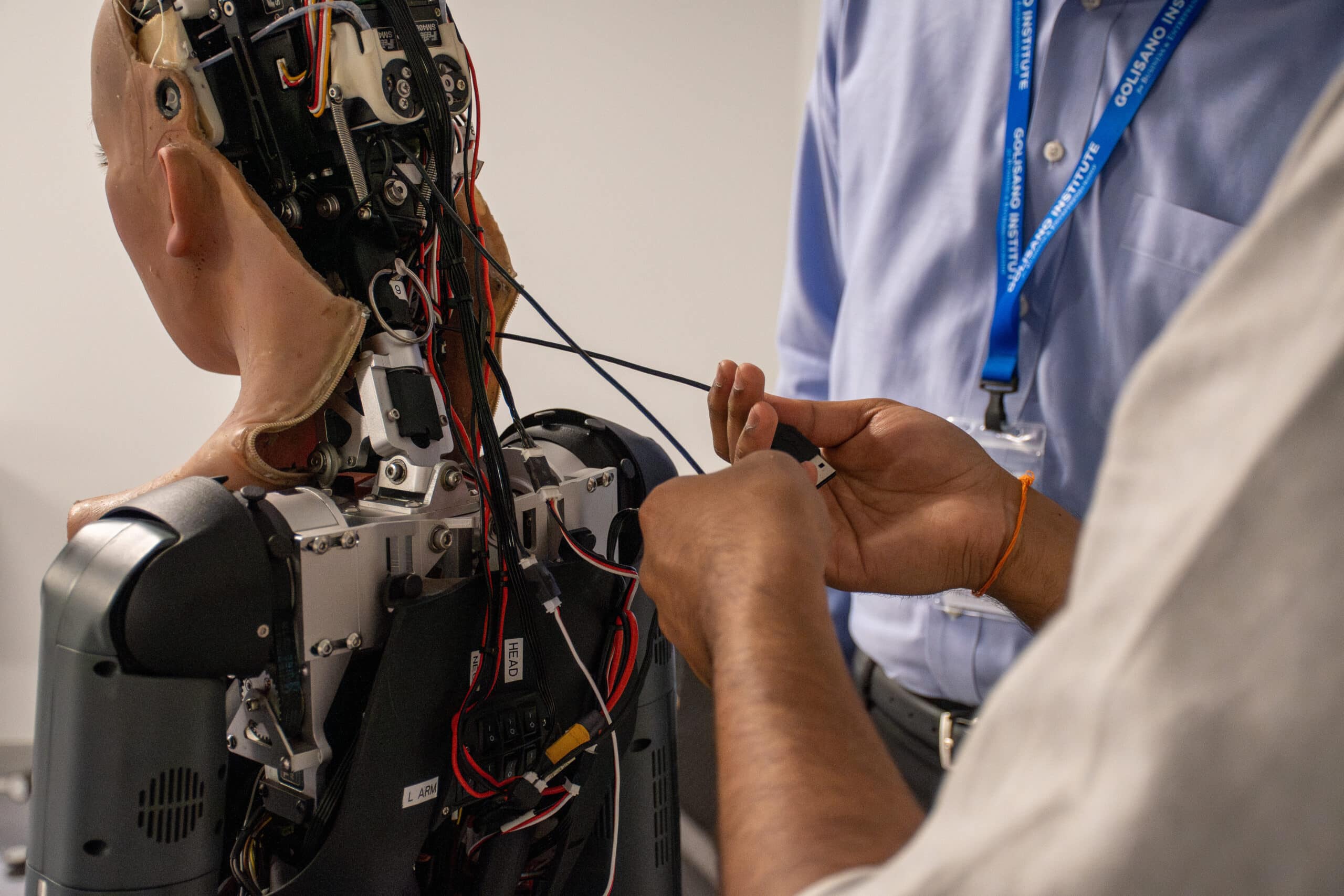 Two technicians work on the back side of a humanoid robot.