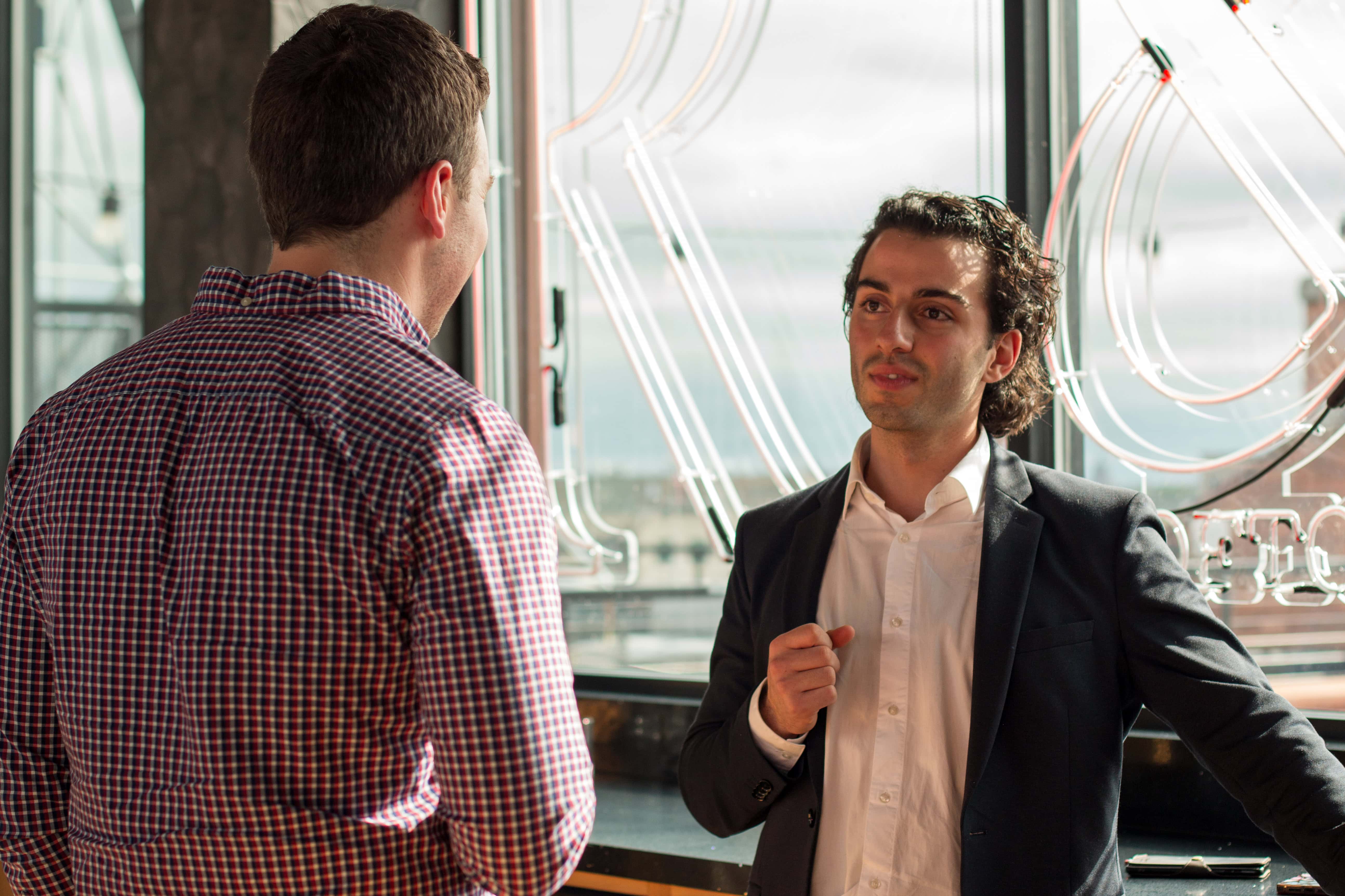 Two men having a conversation in front of a window.