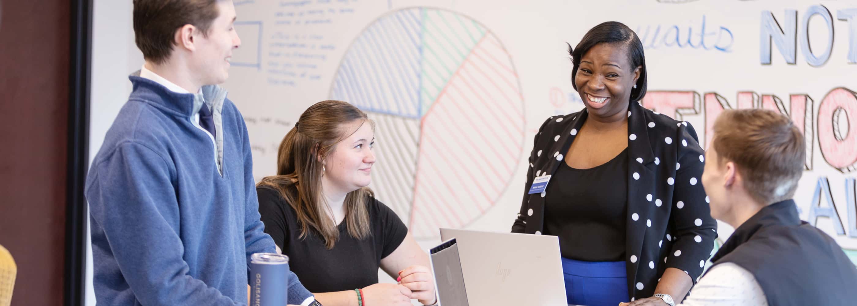 Instructor smiles as she has a conversation with several students.
