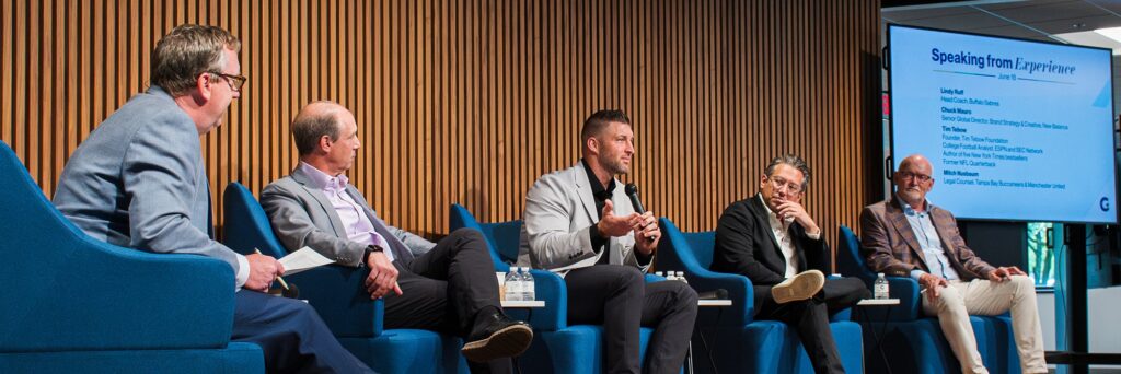 Sports symposium panel presenting while seated on stage.