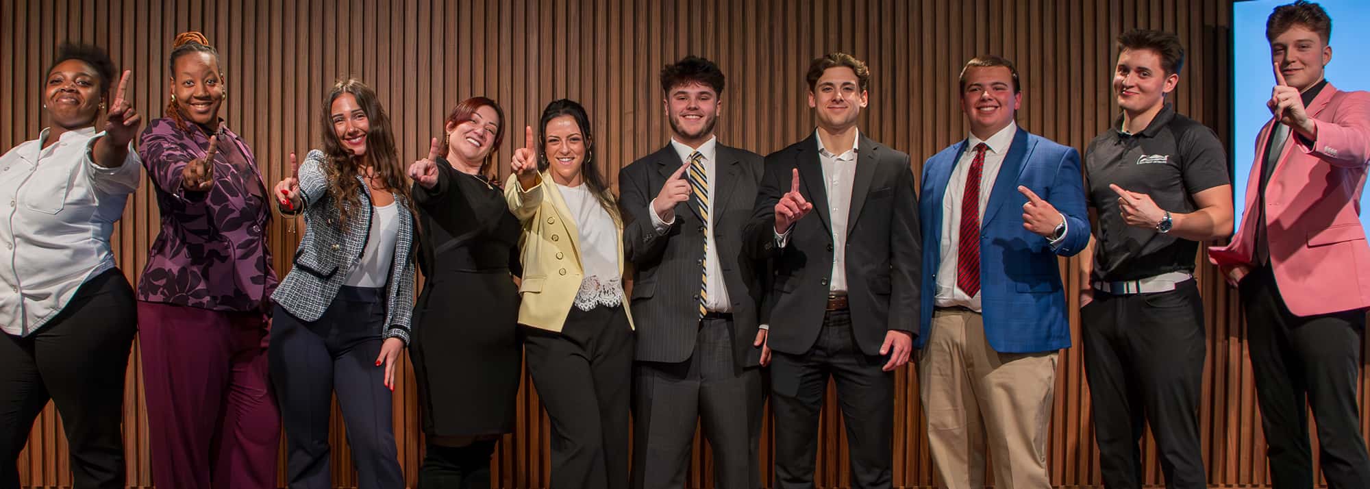 student-experience-number-1-header A group of students standing on stage and smiling with their fingers in the air.