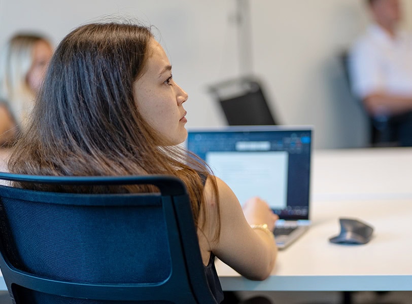 course-offerings-ai Woman sitting in class with her laptop open on the table in front of her.