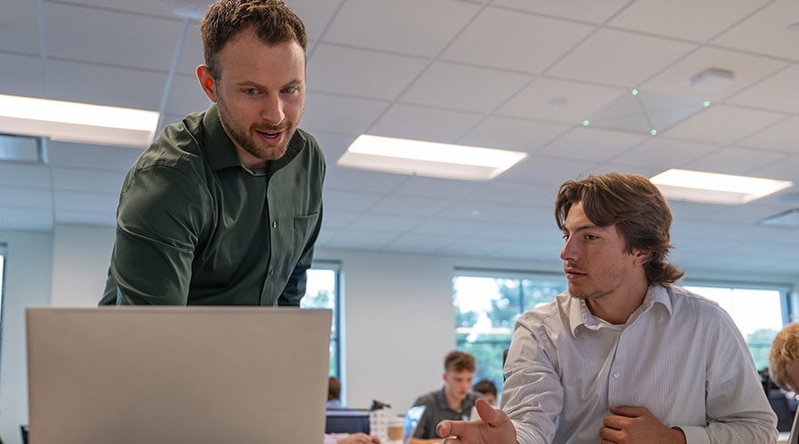 Student and instructor speaking while looking at a laptop.