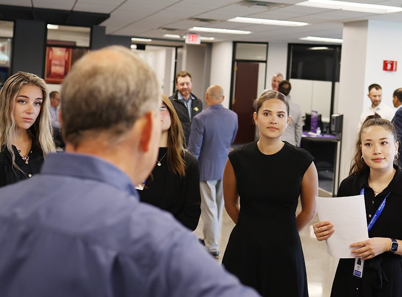 Students speaking with a business leader with his back facing the camera.