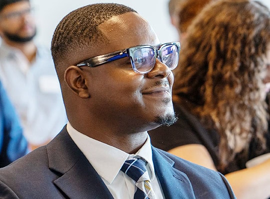 energetic-intern Man in a suit with glasses watching a presentation and smiling.