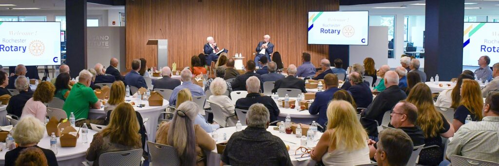 A group sits at round tables in the forum during a presentation.