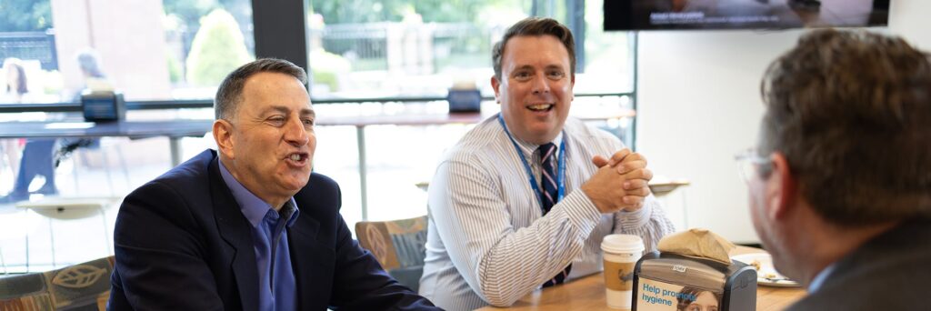 Three men sitting at a table having coffee and talking and laughing.