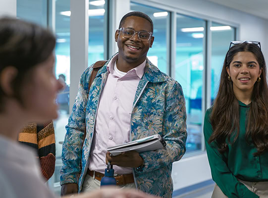 Two students in conversation with a woman who is out of focus and in the foreground.