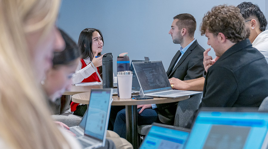 A group of students sitting at tables with laptops open.