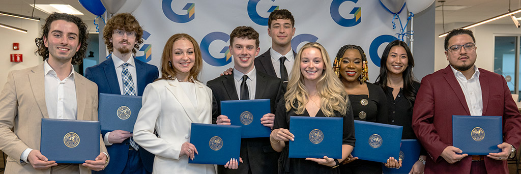 A group of recent graduates posing for a group photo holding their diplomas.