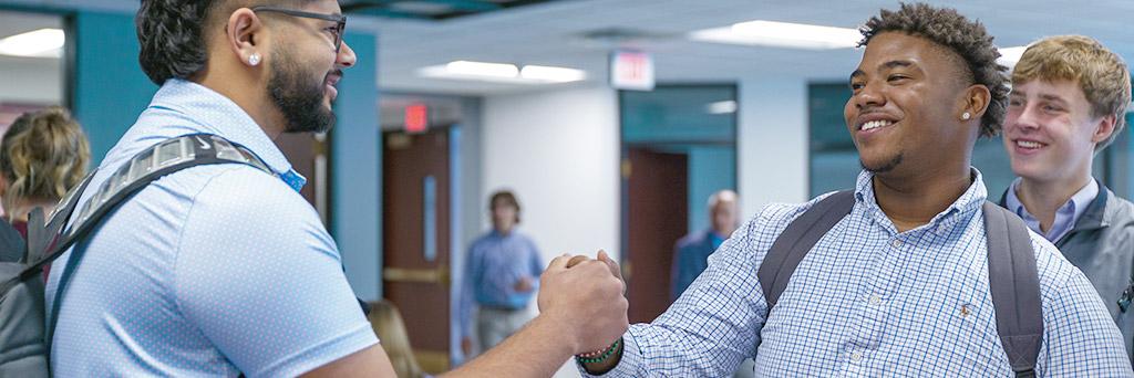 Two students smiling and shaking hands.