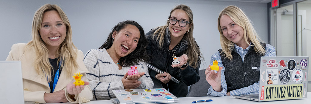 Four students smiling at the camera and showing their miniature rubber ducks.