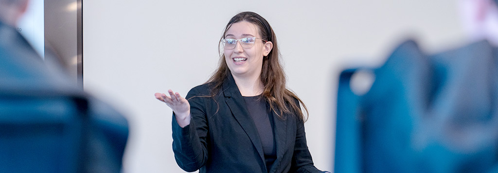 A woman with glasses gestures with her hand while speaking.
