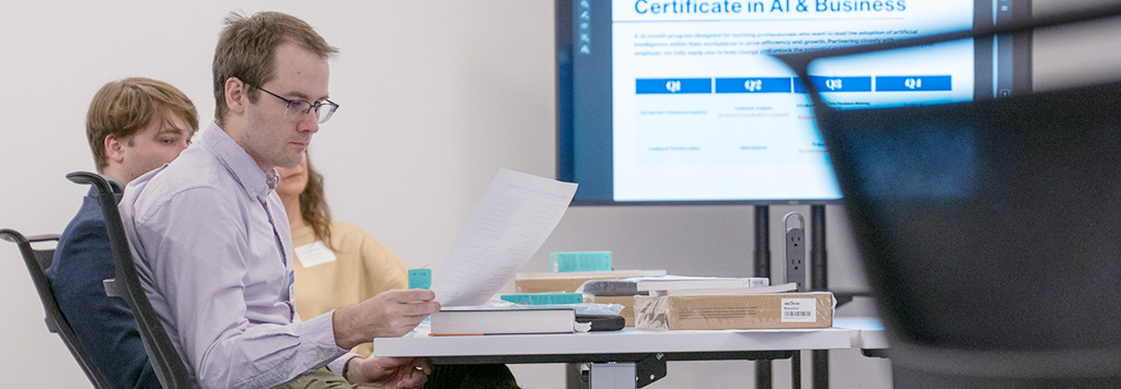 A student reviews a document while sitting at a table in front of a screen