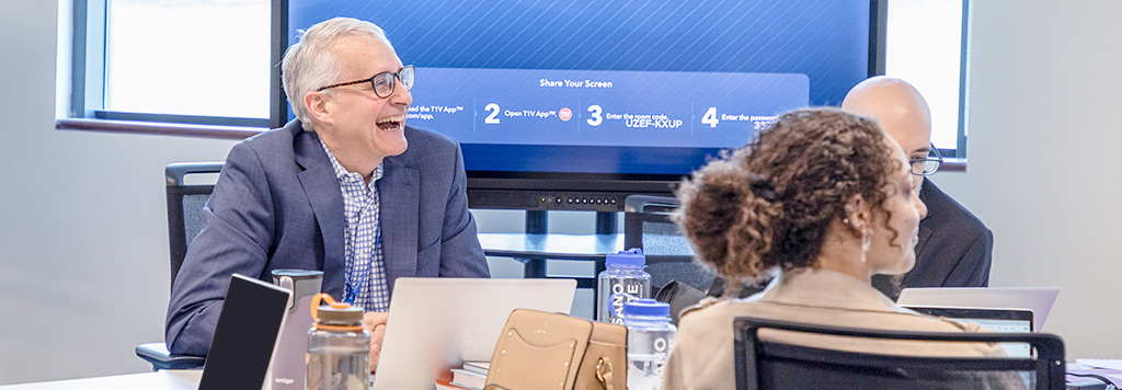 A man laughs while sitting at a table with two other students