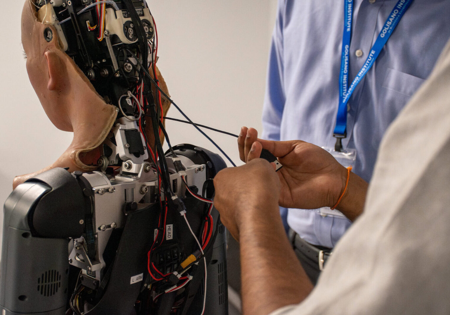 Two technicians work on the back side of a humanoid robot.