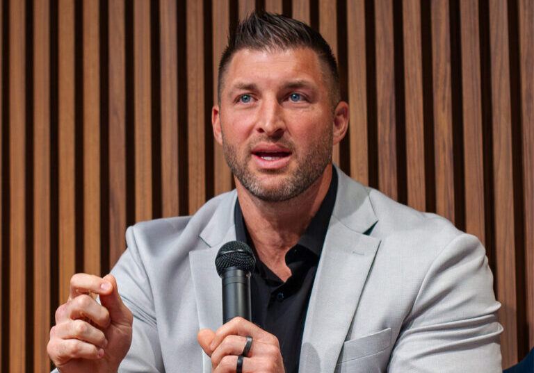 Football legend Tim Tebow speaking with a mic while seated on stage